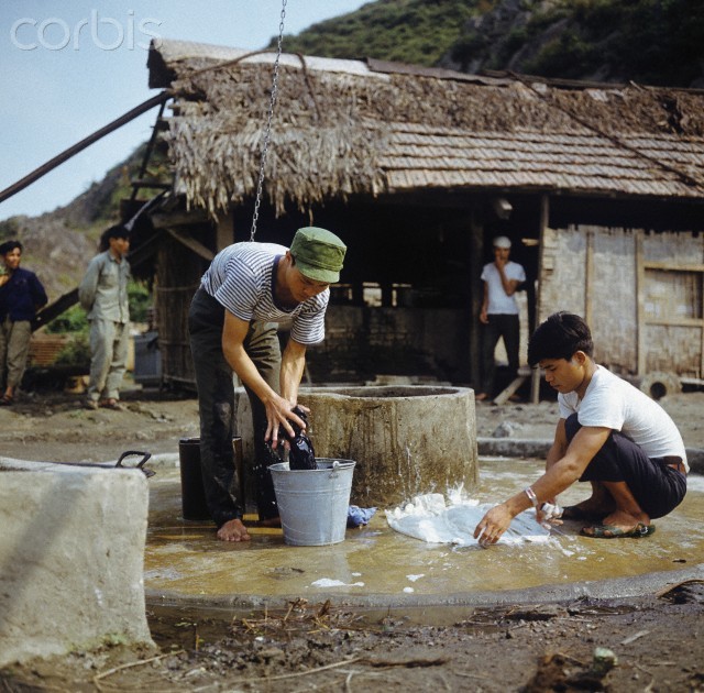 Tháng 3/1973. Hai thanh niên đang giặt bên một giếng nước trên phố Khâm Thiên. Phía sau là một căn lều dựng tạm sau trận bom B52 năm 1972. Ảnh. © Werner Schulze-dpa-Corbis.